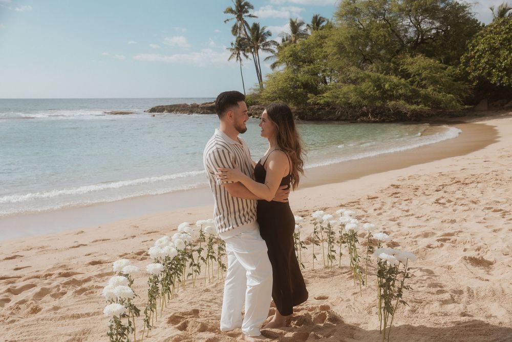 Romantic couple embraces on a tropical beach with palm trees and ocean waves in the background.