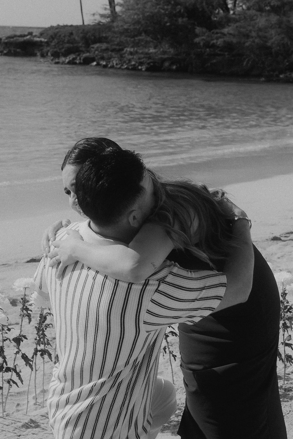 Black and white photo of a couple in intimate moment on a scenic beach surrounded by palm trees.