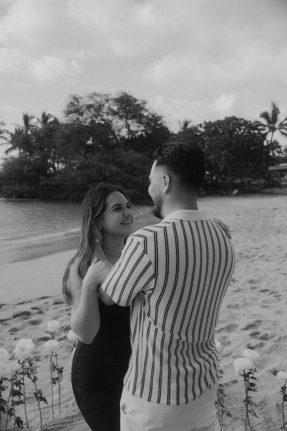 Couple sharing romantic moments on a tropical beach with palm trees in the background.