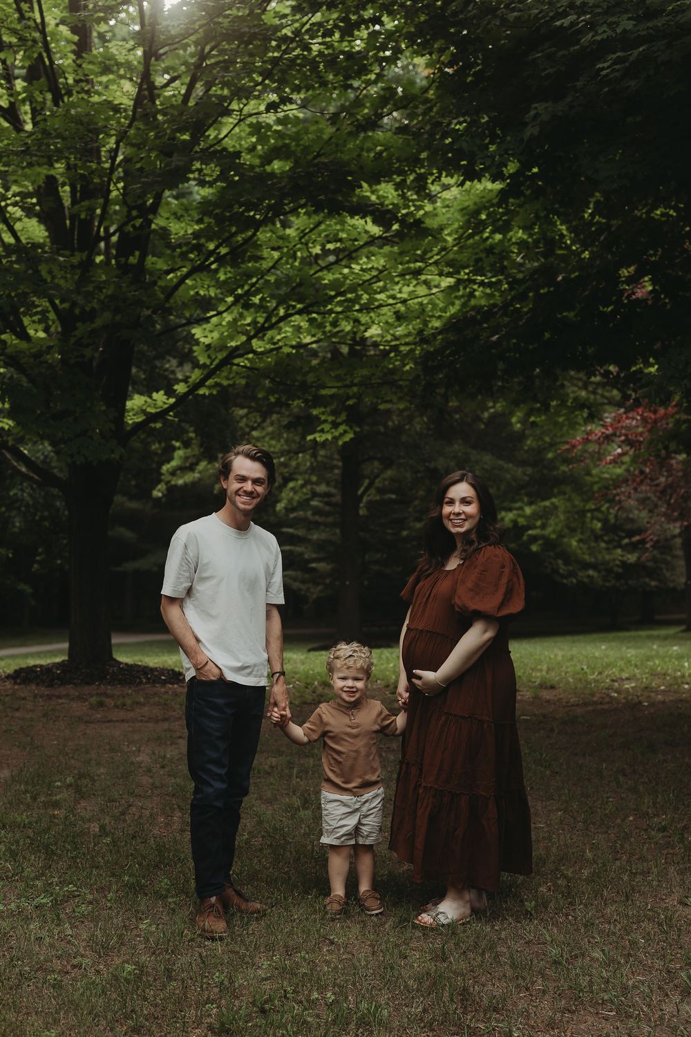 Family group standing together in a wooded area with lush green trees and natural lighting.
