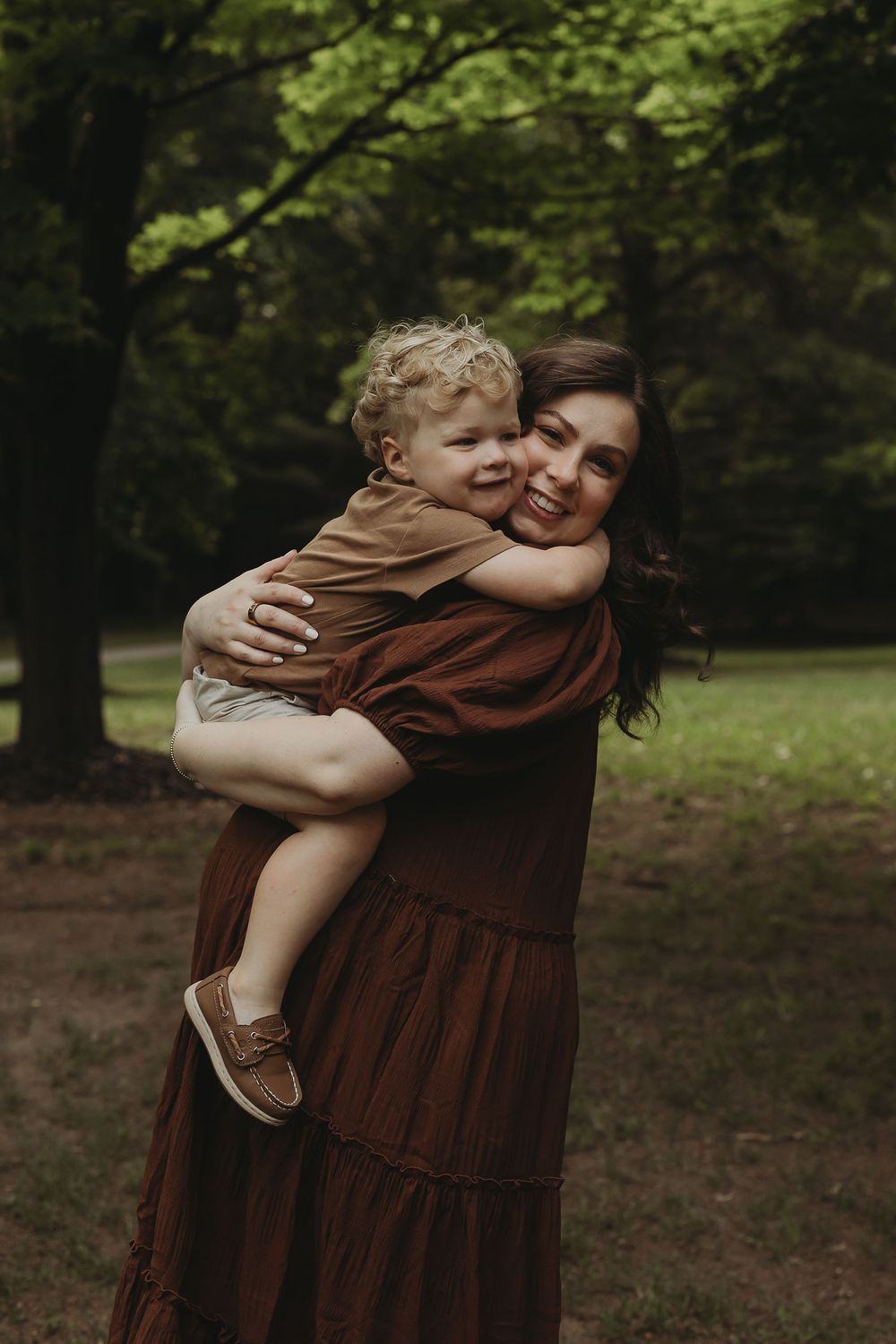 An affectionate embrace between parent and young child in a wooded outdoor setting with lush greenery.
