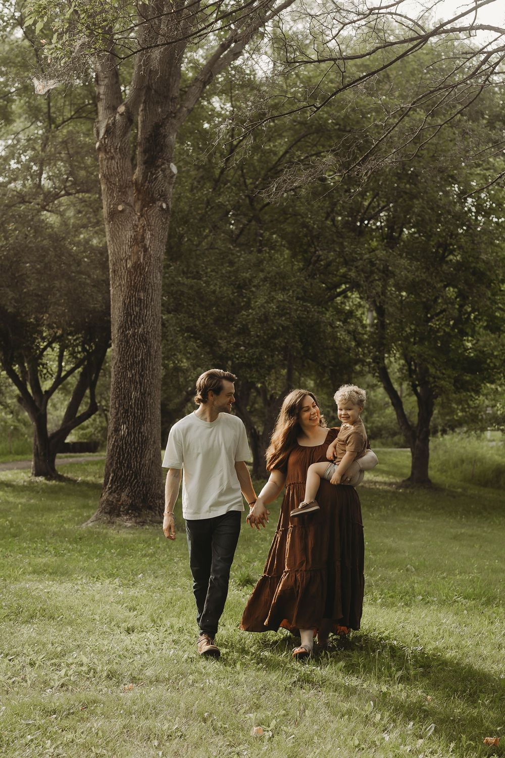 A group walks together through a rustic wooded area wearing vintage-inspired dresses and casual attire.