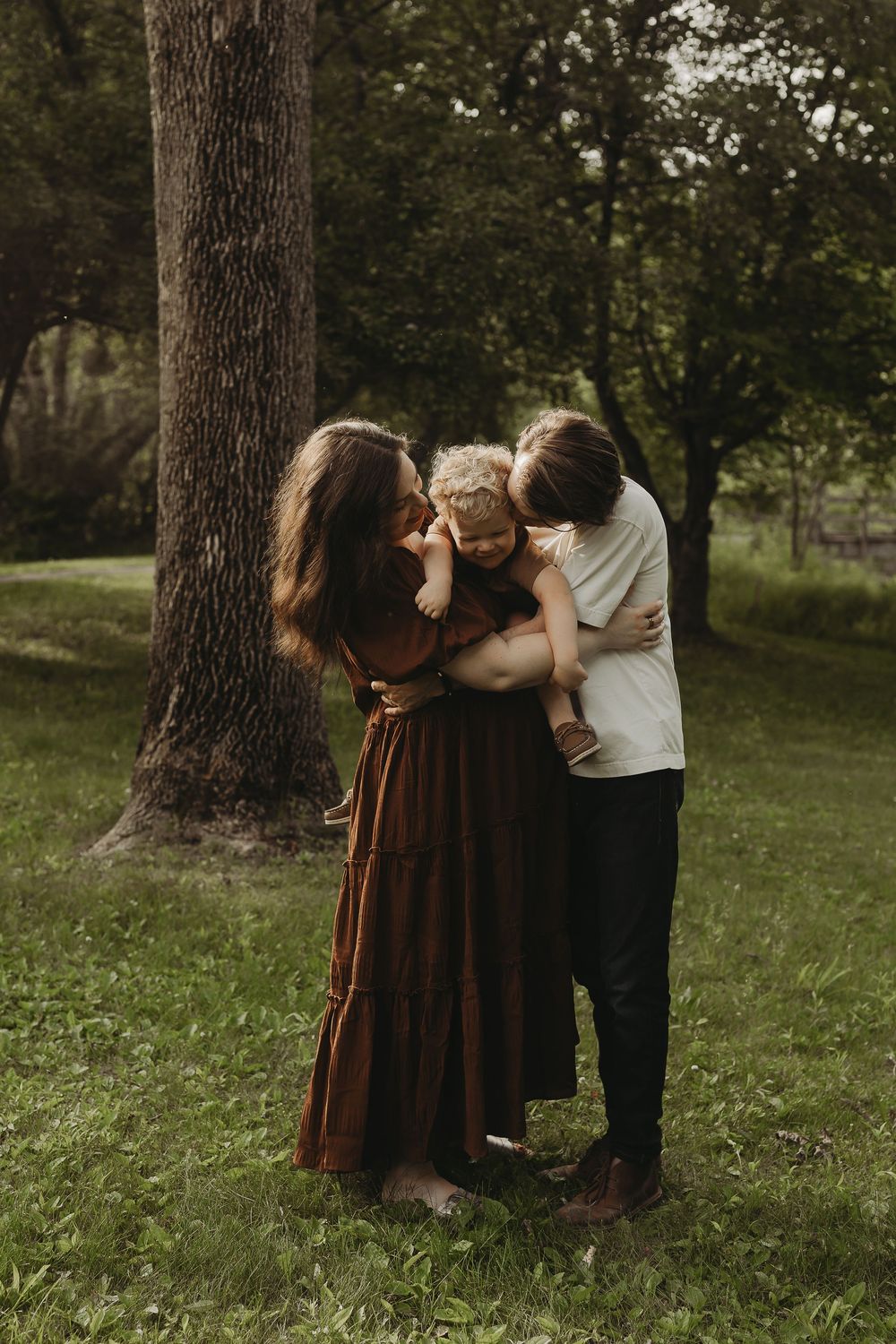 A tender family moment captured beneath a large tree in a peaceful park setting.