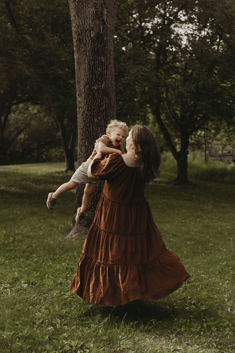 Dancing couple in coordinated brown outfits spins gracefully across a grassy outdoor setting during golden hour.