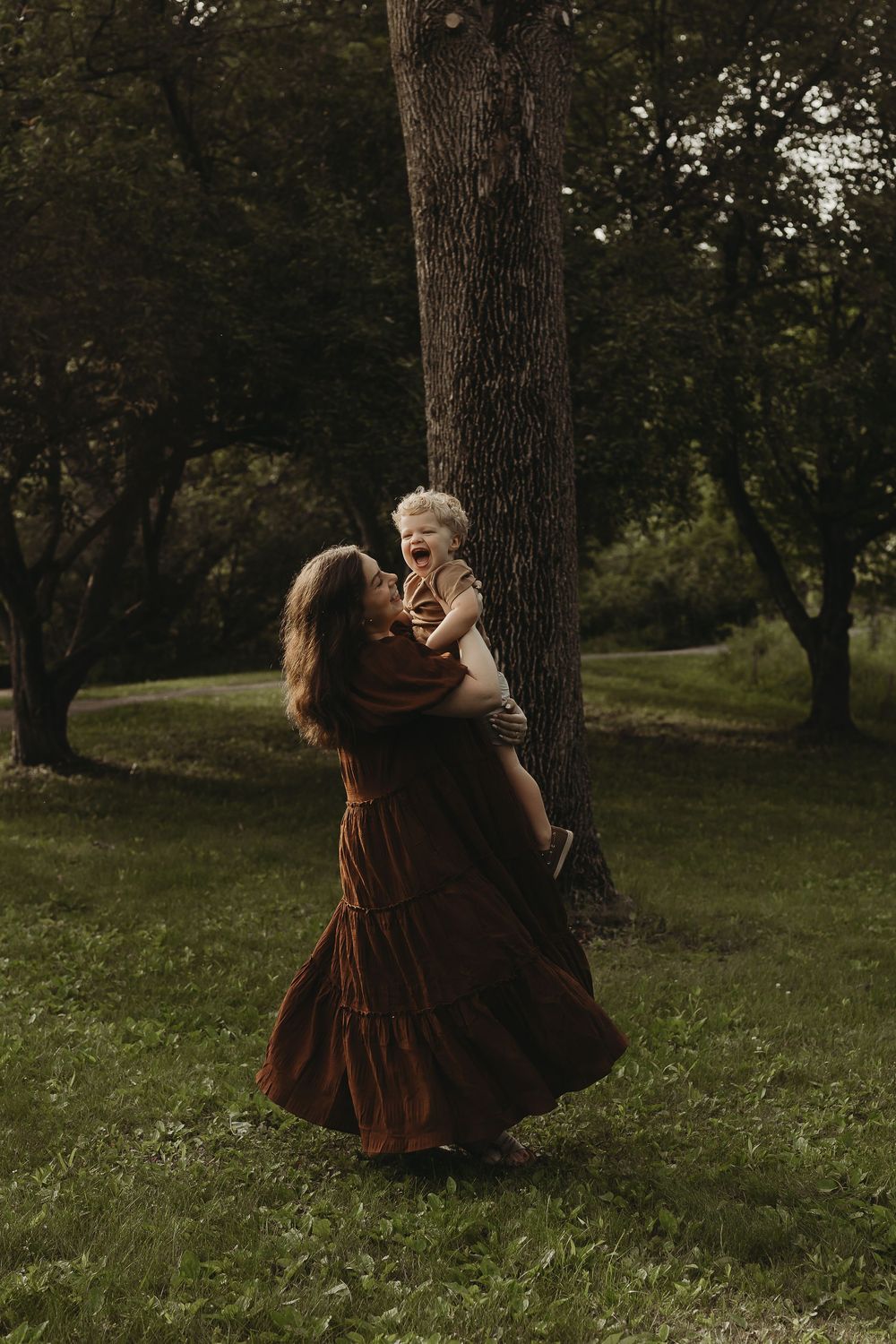 A loving moment between parent and child dancing together in a grassy woodland setting at sunset.