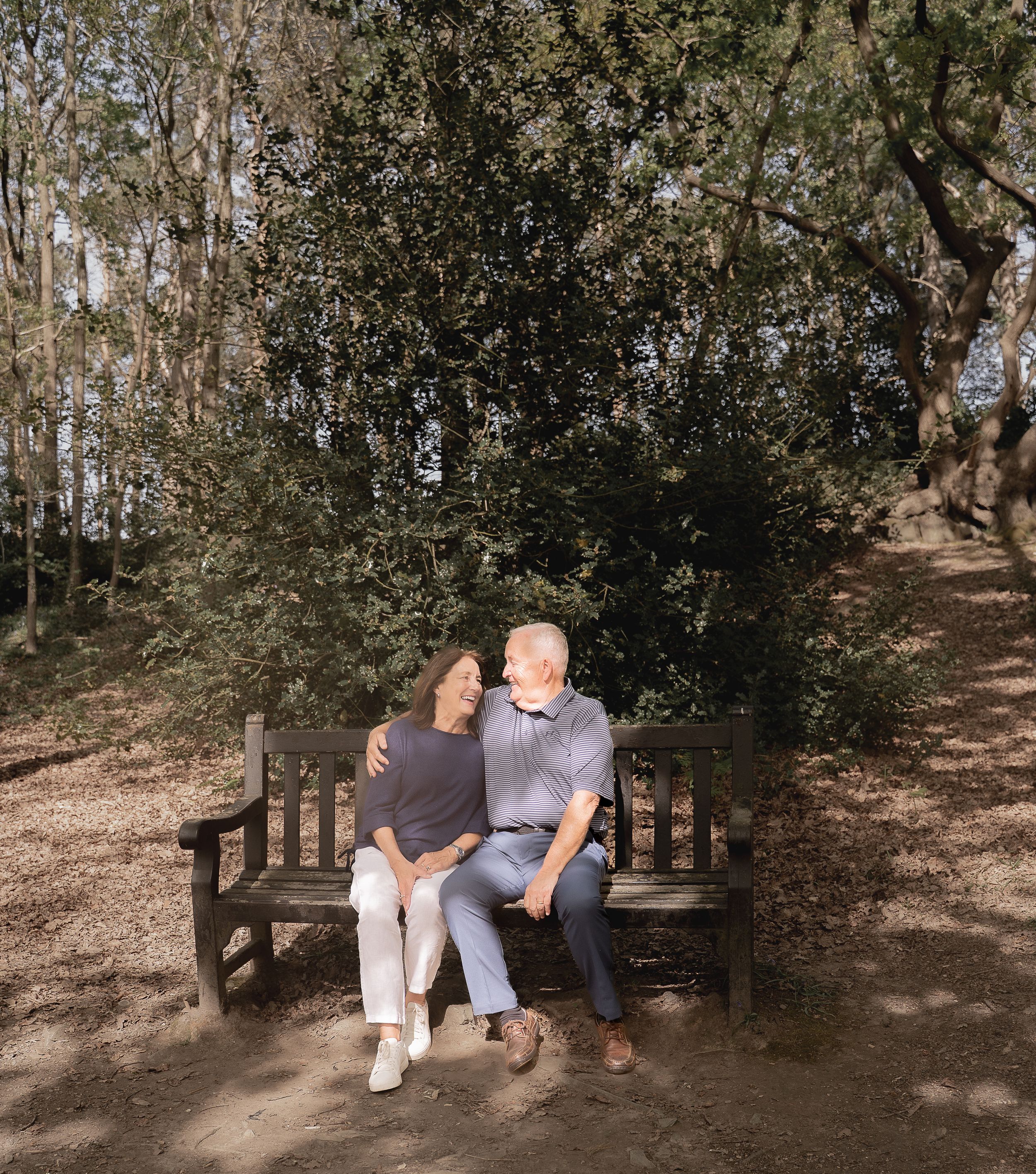 Two people share a tender moment while sitting together on a wooden bench in a serene wooded setting.