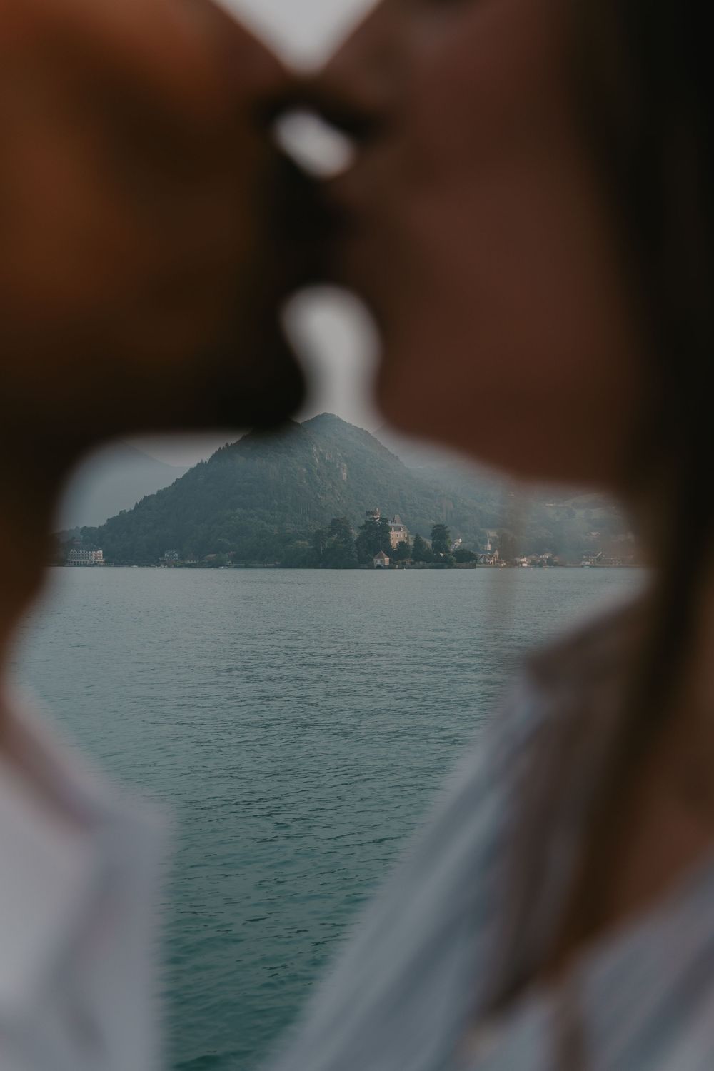 Avant-plan flou encadrant un lac de montagne à Annecy, créant une atmosphère calme et contemporaine. Photographe Annecy couple
