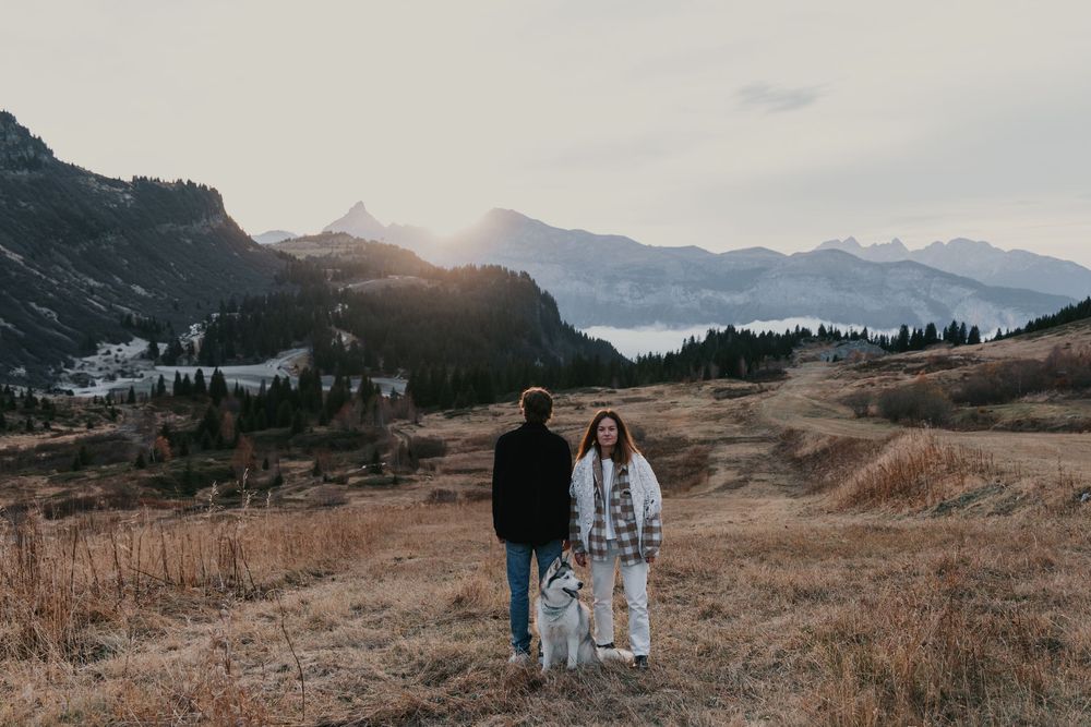 Couple marchant dans un paysage de montagne au coucher du soleil avec une lumière dramatique des sommets en arrière-plan.