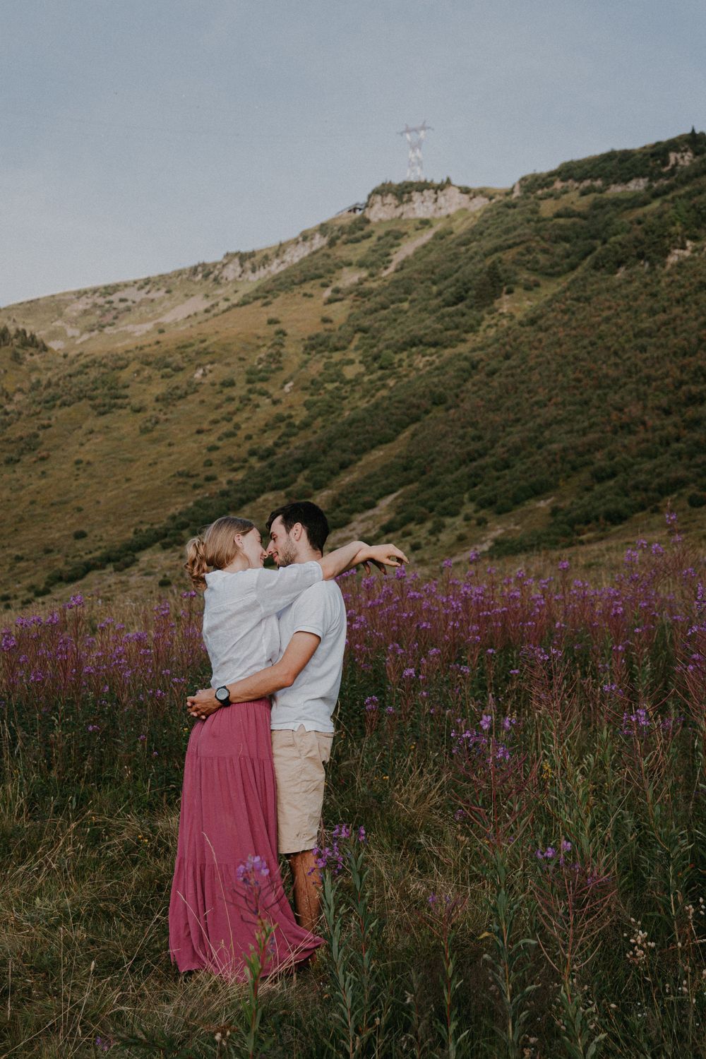 A couple embraces in a field of purple wildflowers with mountains in the background.
