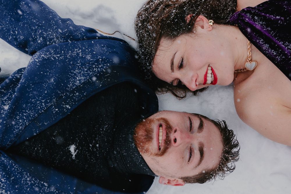 A couple laughs together while lying down against a dark starry background.