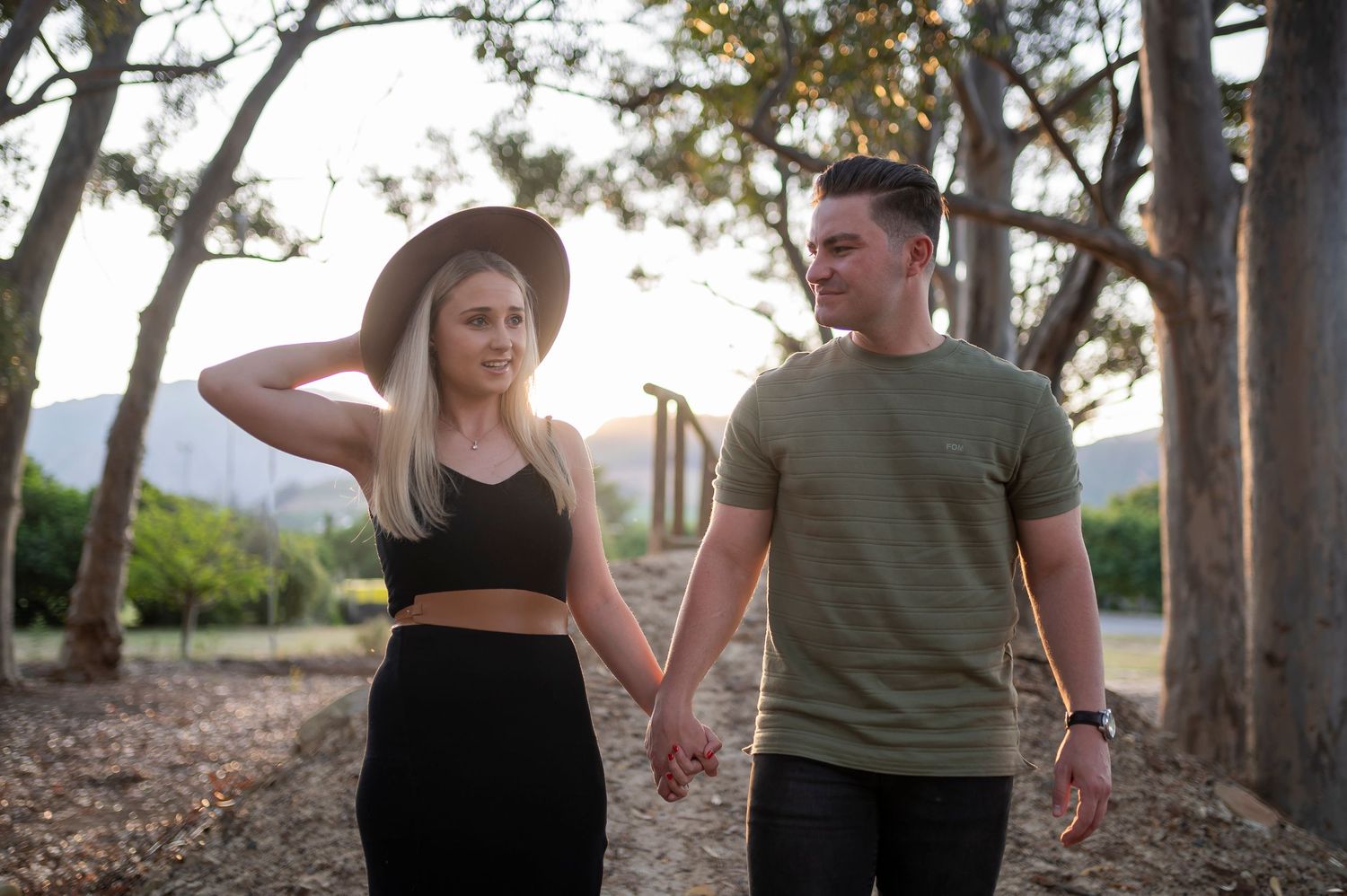 A couple poses together in a rustic outdoor setting during sunset with trees in the background.