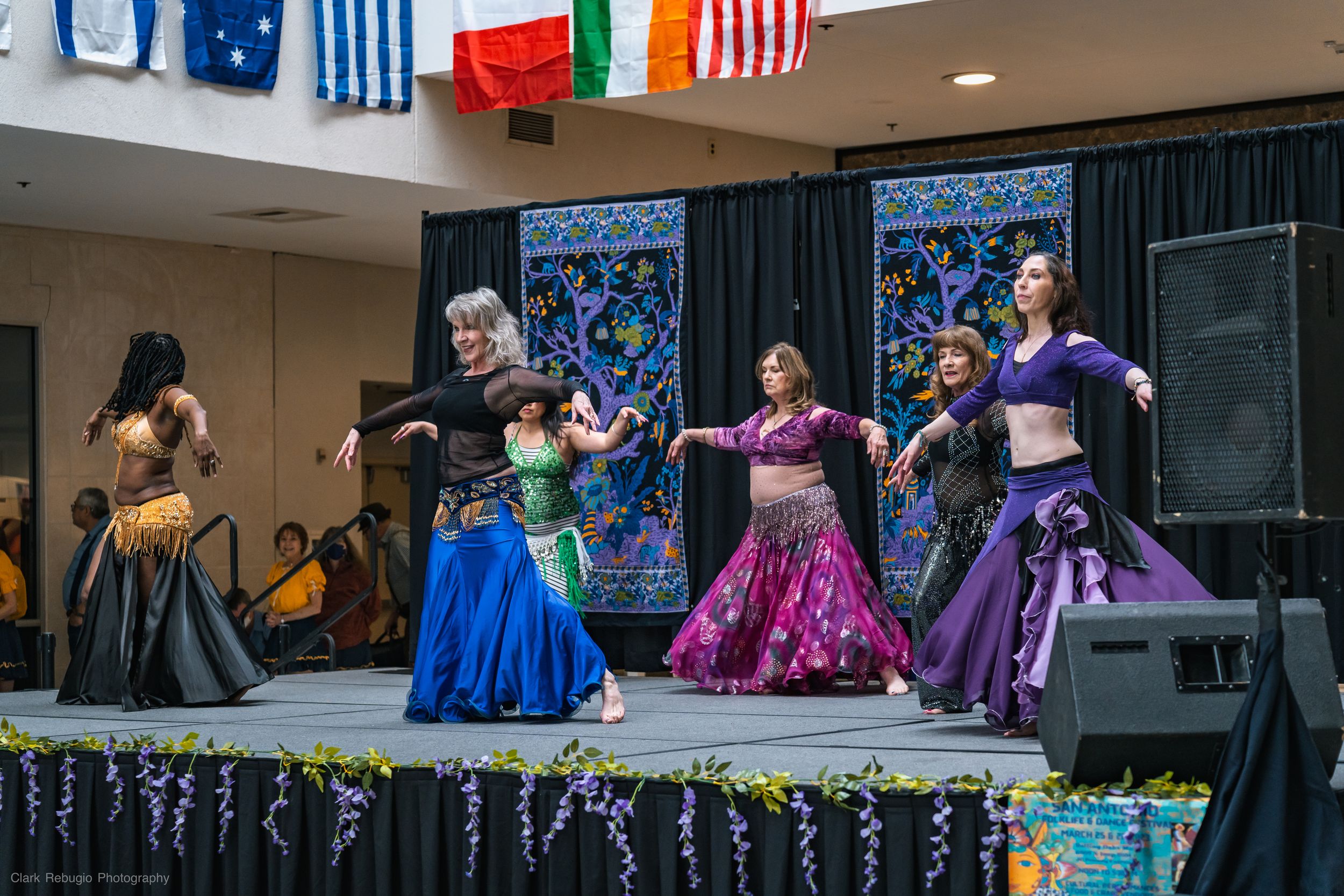 Group of belly dancers in vibrant skirts and tops performing a Middle Eastern-inspired dance at a community celebration.