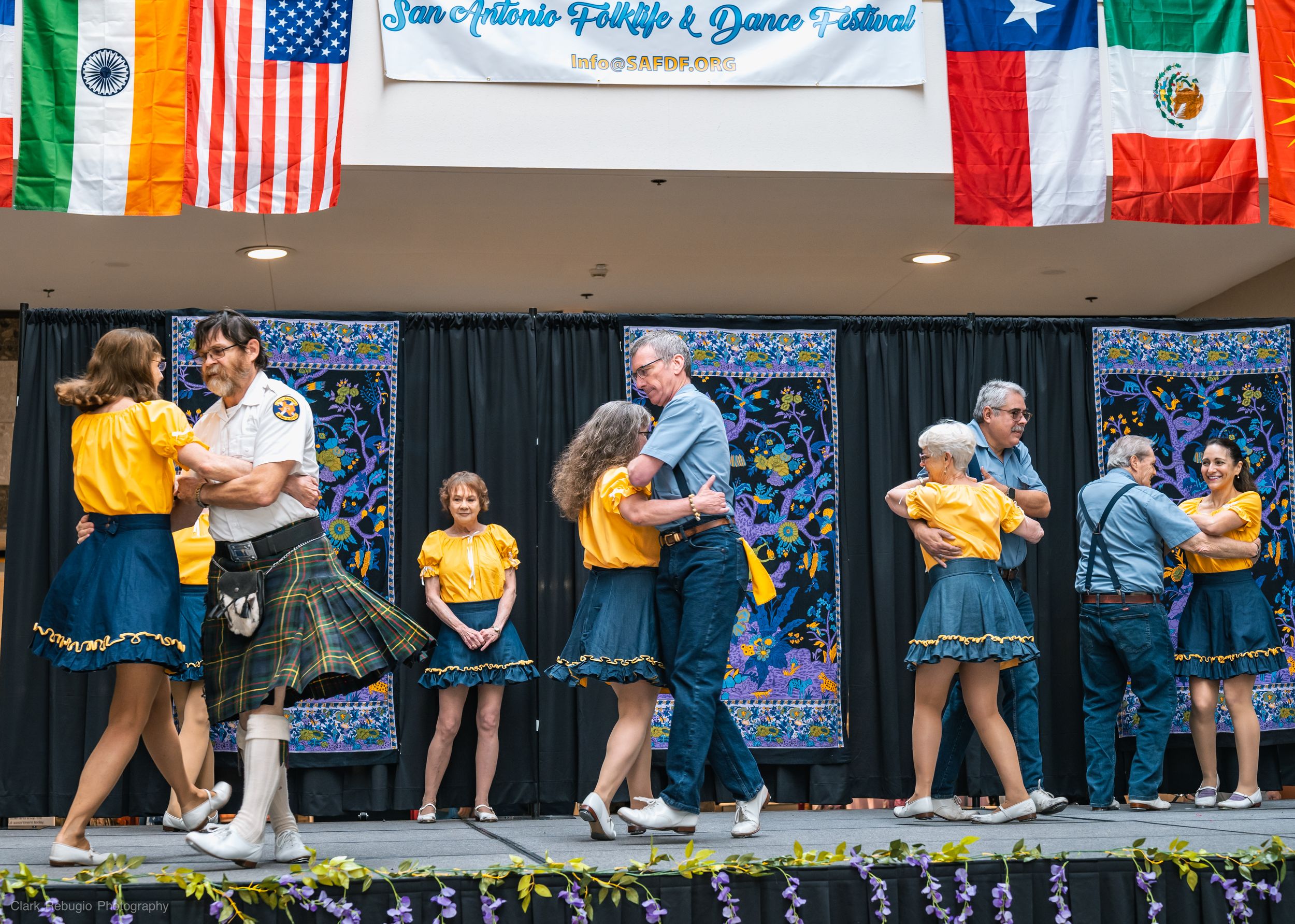 Couples in coordinated yellow and blue outfits performing a traditional American folk dance at a multicultural event.