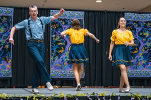 Group of dancers in blue jeans and yellow shirts performing a lively country-western style dance on stage at a cultural festival.