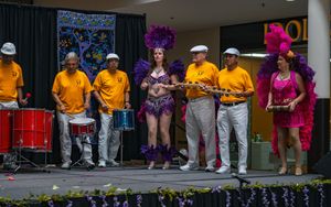 Brazilian-style percussion band in yellow shirts with samba dancers in colorful costumes performing together at a multicultural event.