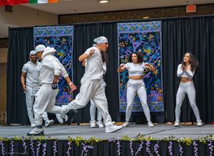 Group of performers dressed in all white dancing energetically on stage during a lively cultural festival show