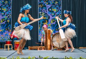 Polynesian dancers in blue costumes performing a traditional drum and dance routine on stage at a cultural festival.