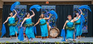 Filipino dancers in turquoise blue dresses performing a graceful fan dance with live drumming at a multicultural festival.