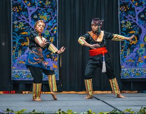 Traditional Filipino warrior dance performed by two dancers in black and gold costumes with bamboo sticks on stage at a cultural celebration