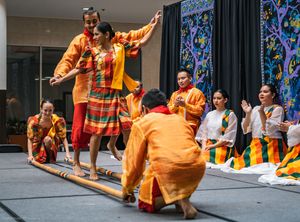 Filipino folk dancers performing the traditional tinikling bamboo dance in colorful costumes on stage at a multicultural event.