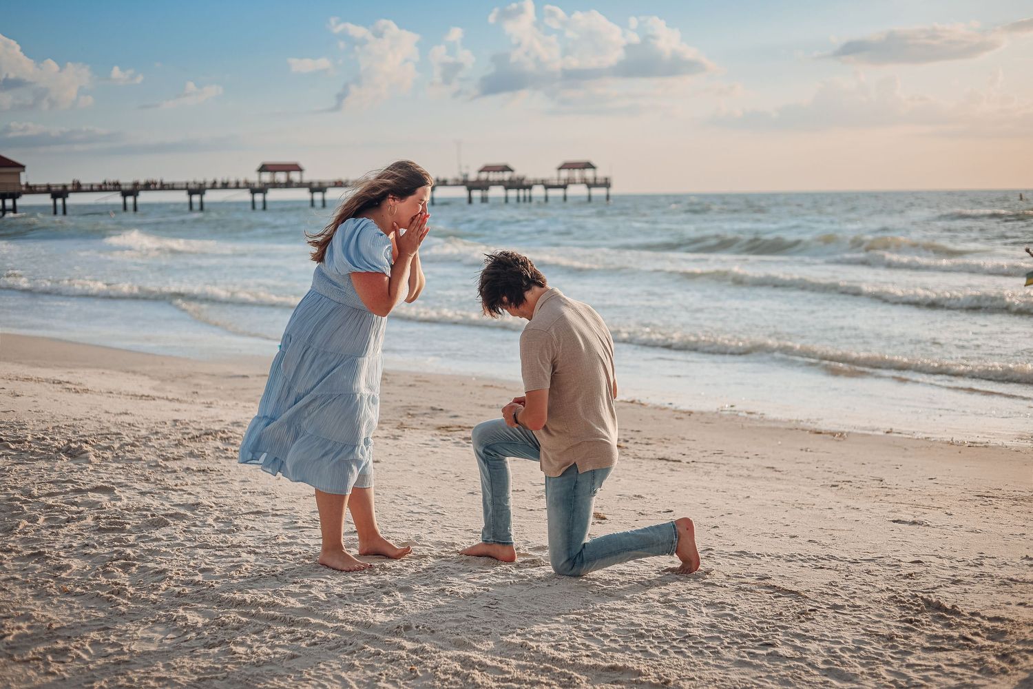 Romantic beach proposal scene at sunset with pier and ocean waves in background. Proposal photography