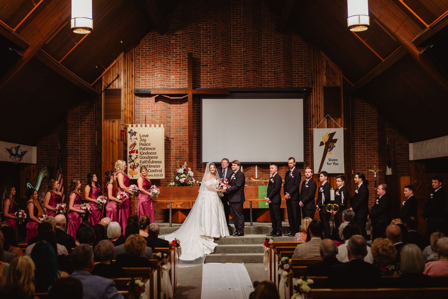 Wedding ceremony taking place in a rustic wooden church with exposed beams and hanging pendant lights.