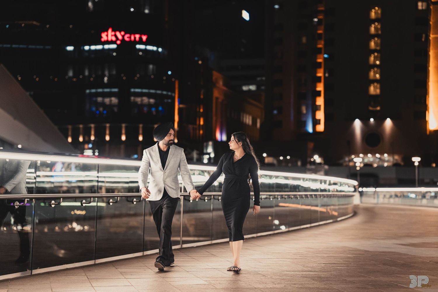 Two people walking at night along an illuminated urban pathway beside glowing modern architecture.