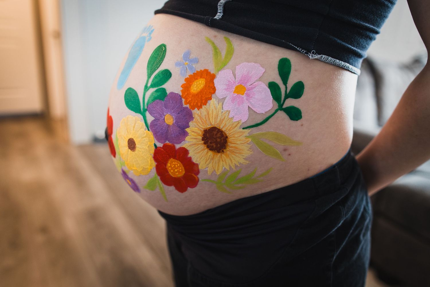 Close-up of a painted pregnant belly featuring colorful flowers and foliage.