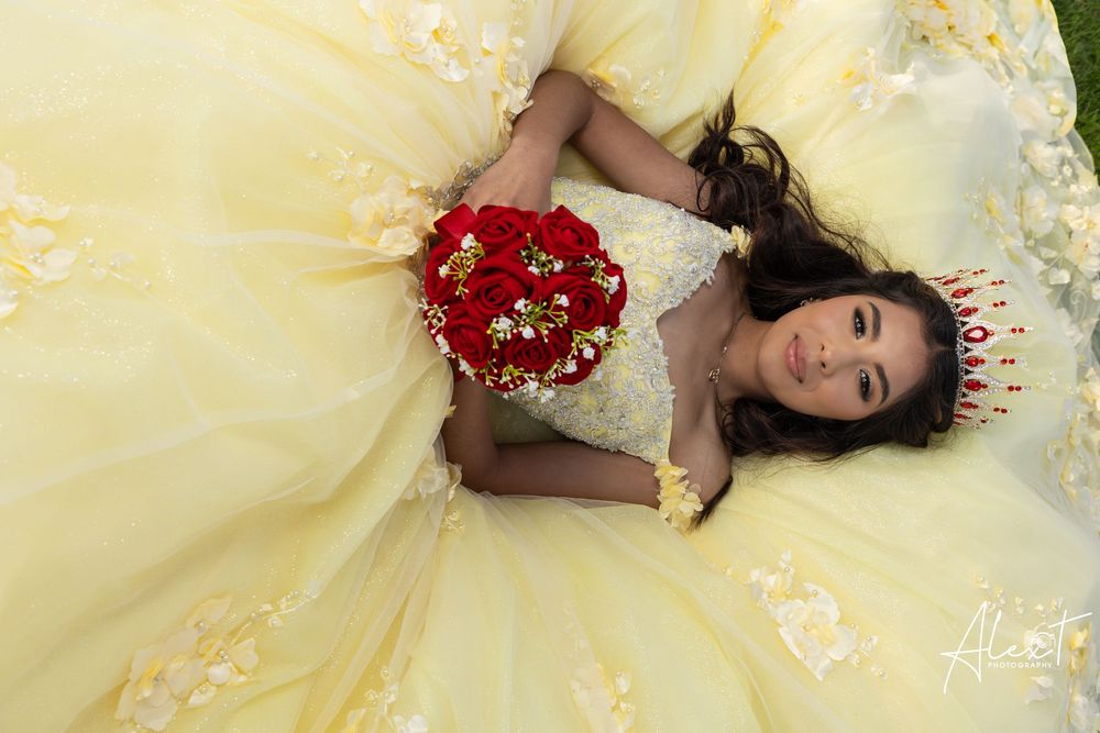 Overhead portrait of Quinceañera Aileen lying in her yellow gown with a red rose bouquet. Creative XV photography by Alex T in Waukegan.