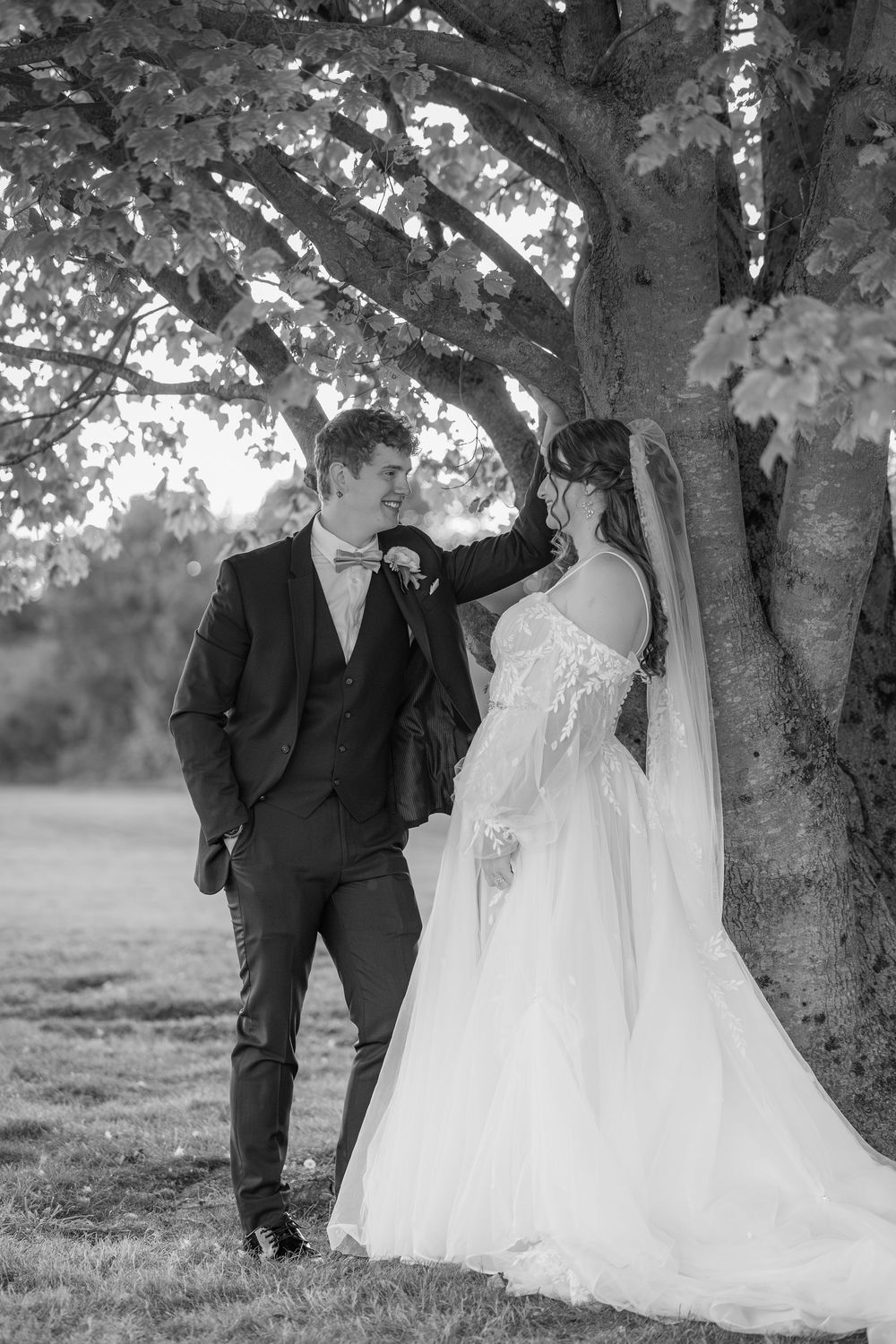 Elegant black and white wedding photography series of a couple walking and embracing under a large tree.