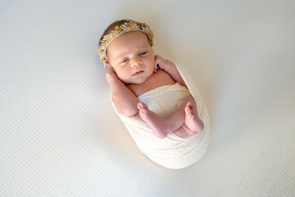 A sequence of professional newborn photography shots showing a sleeping baby in soft white wraps against light backgrounds.