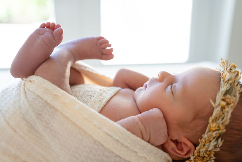 Adorable sleeping newborn baby rests against misty white blankets in a studio setting.
