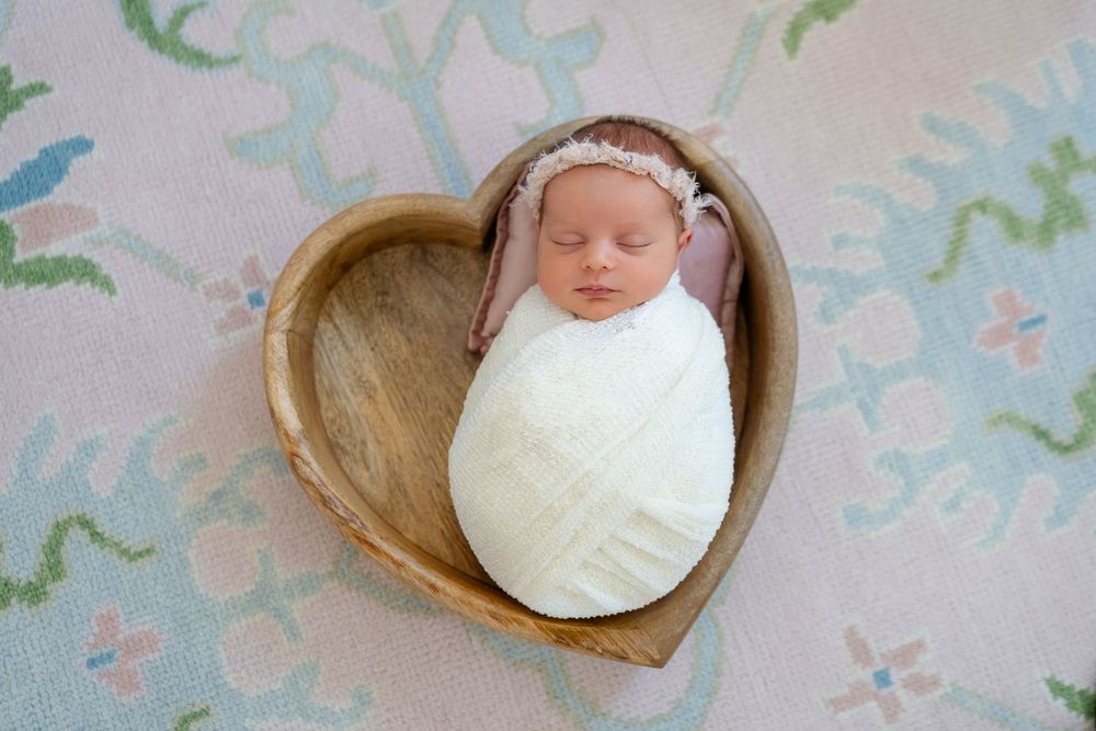 Tiny newborn baby sleeping peacefully on white blanket with soft floral background details.