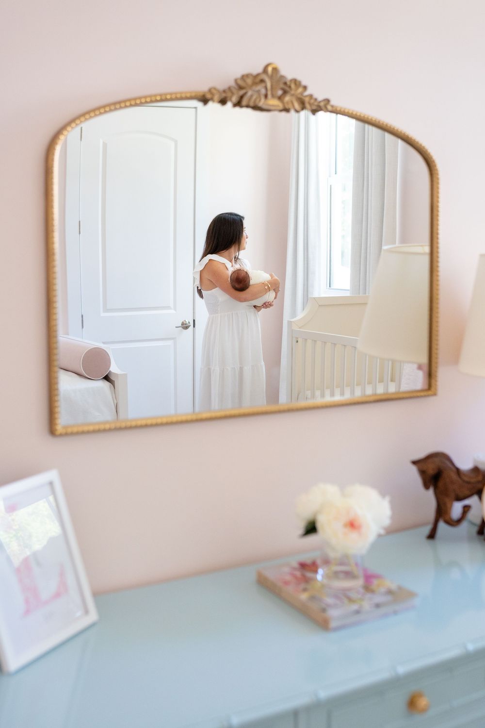 Four similar arched gold mirrors mounted on a light pink wall above a pale blue shelf with decorative items.