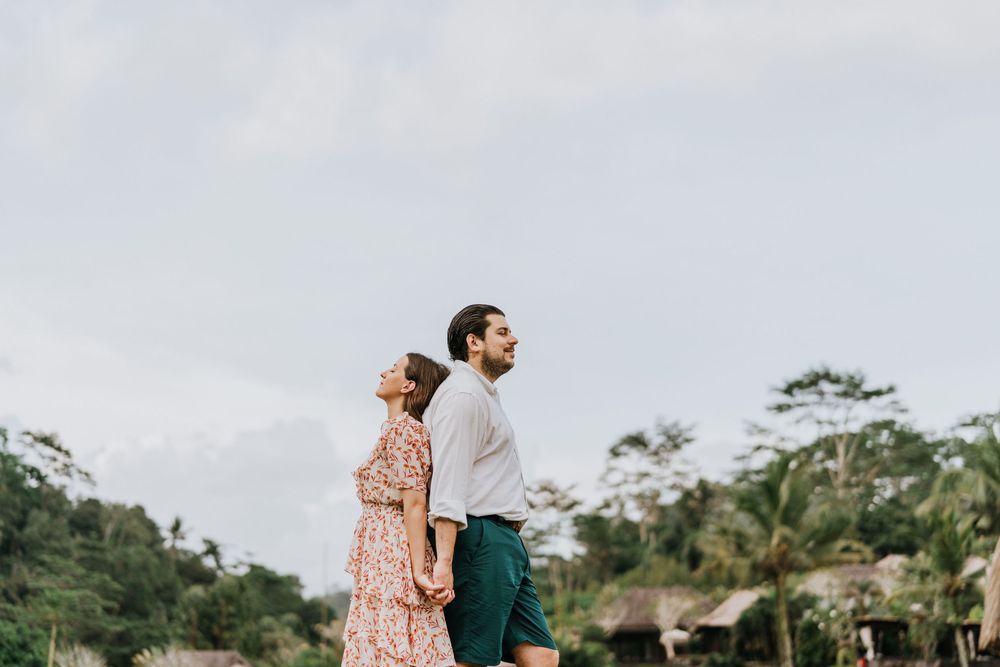 A couple enjoys the view from a tropical hillside with bamboo structures visible.