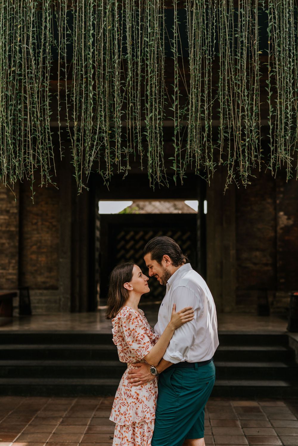 A romantic scene under hanging vines in an atmospheric indoor setting.