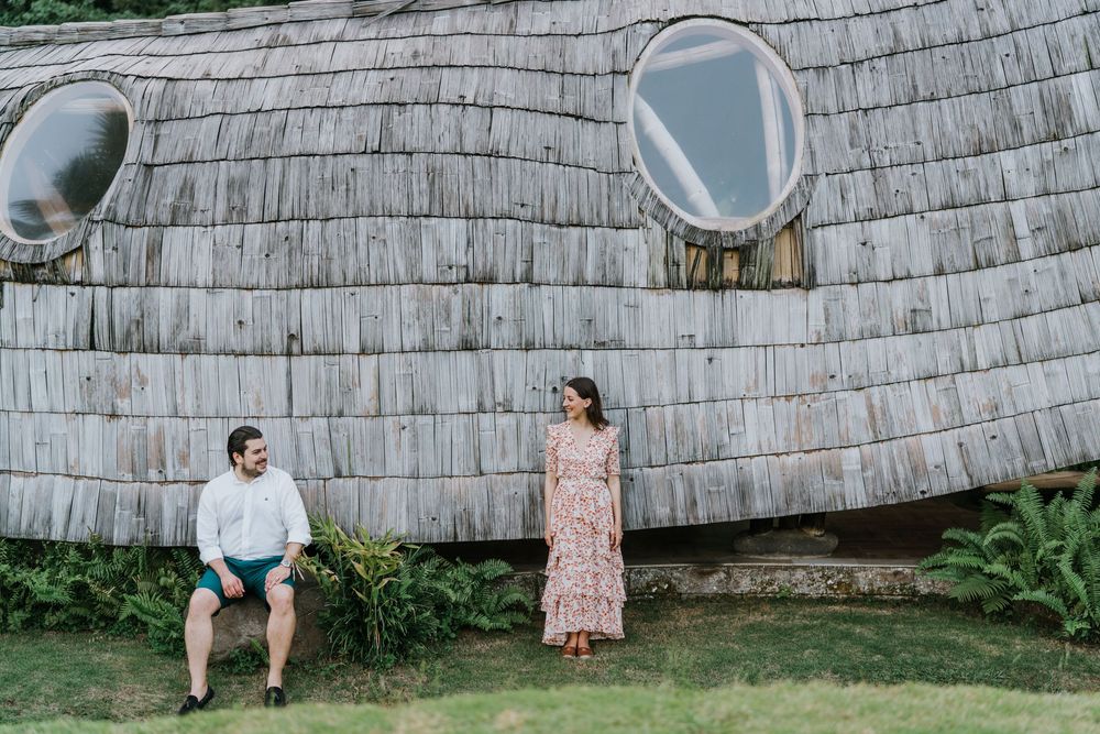 A couple poses against a curved wall with oval windows in a tropical setting.