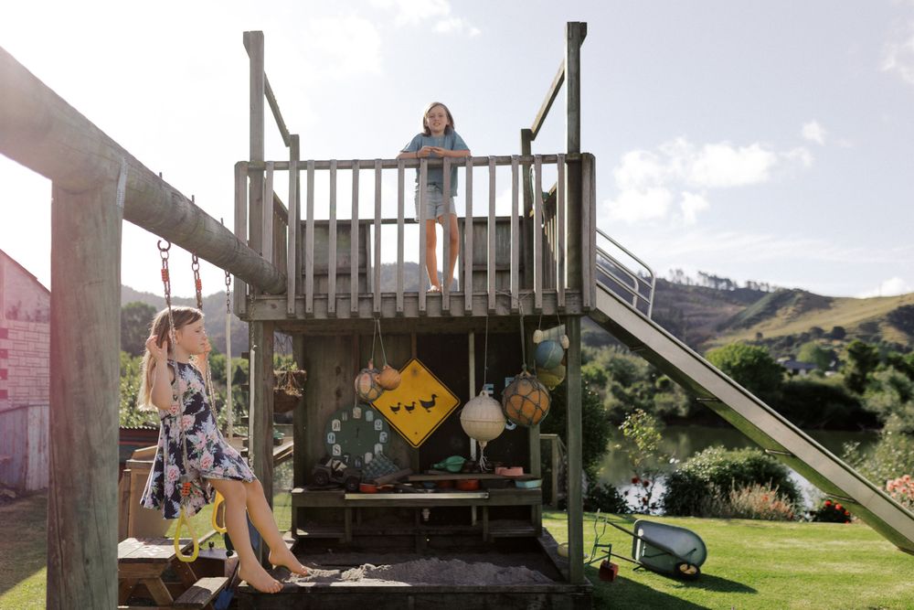 An adventurous young person crosses a wooden suspension bridge over a grassy valley in sunny outdoor scenery.