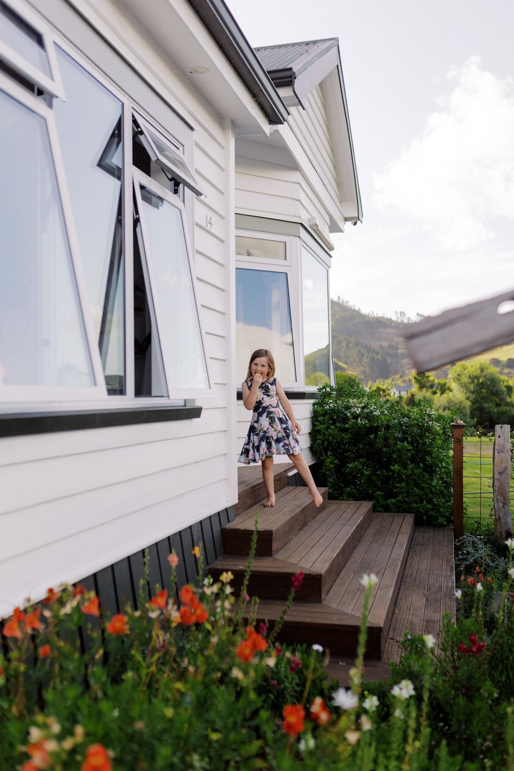 Three connected photos show a wooden deck with blooming orange flowers in front of white building walls and windows.