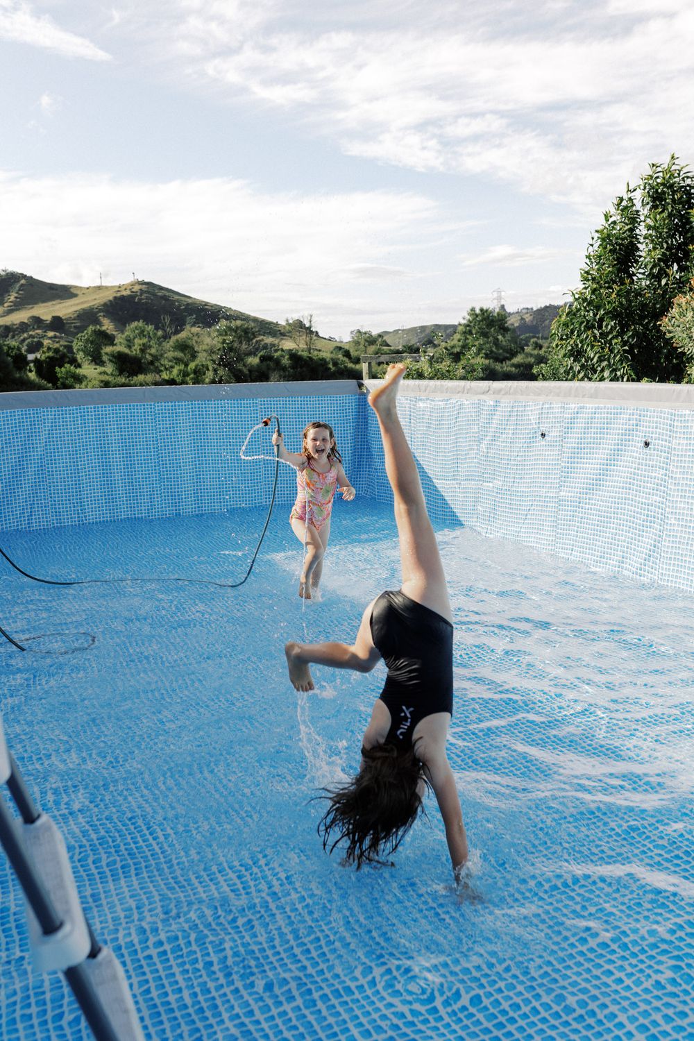 A sequence of photos showing a person doing backflips and somersaults into a blue swimming pool with mountains in background.