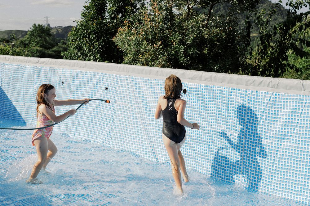 People enjoying and playing in a bright blue swimming pool on a sunny day.
