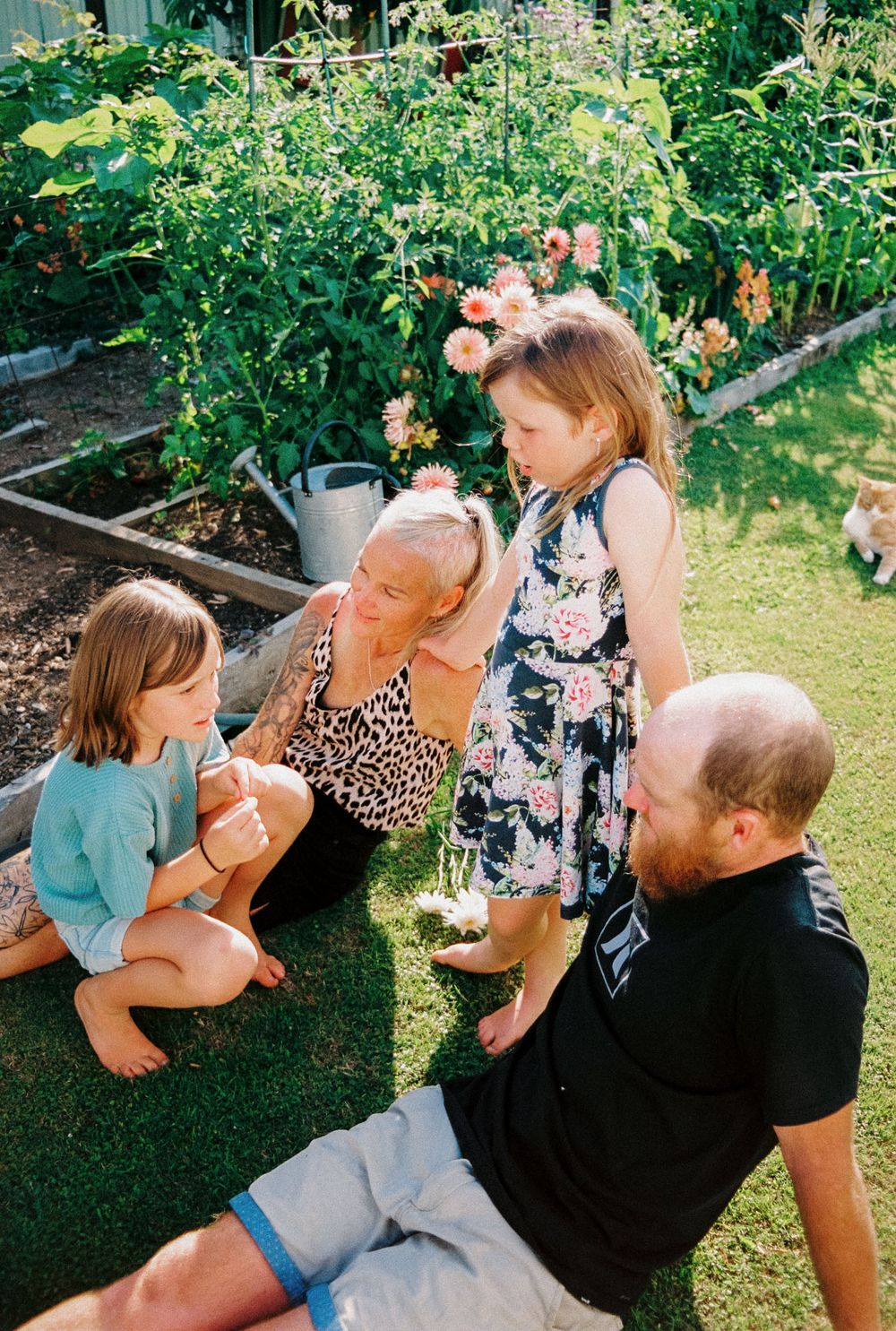 A family gathering in a flourishing vegetable garden with flowering plants and a watering can.