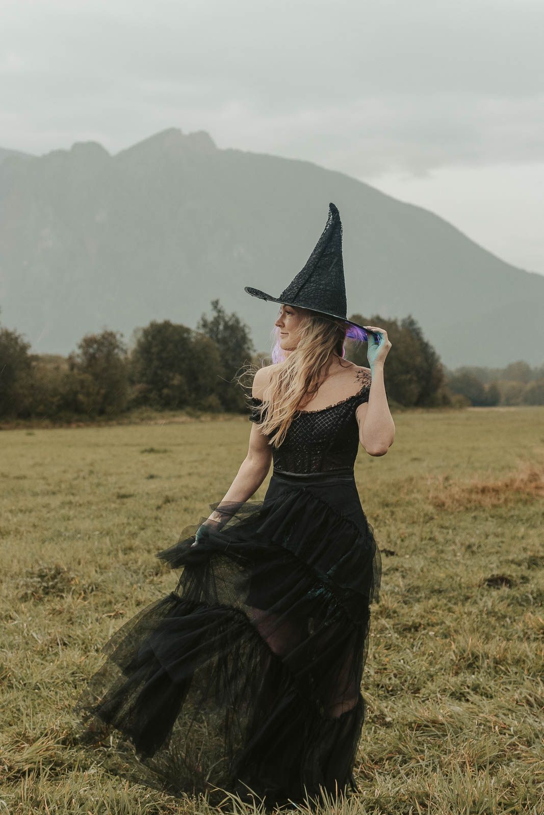 Spooky Halloween couple photoshoot with woman in black top and jeans turning away as masked figure approaches in a foggy field. spokane wa