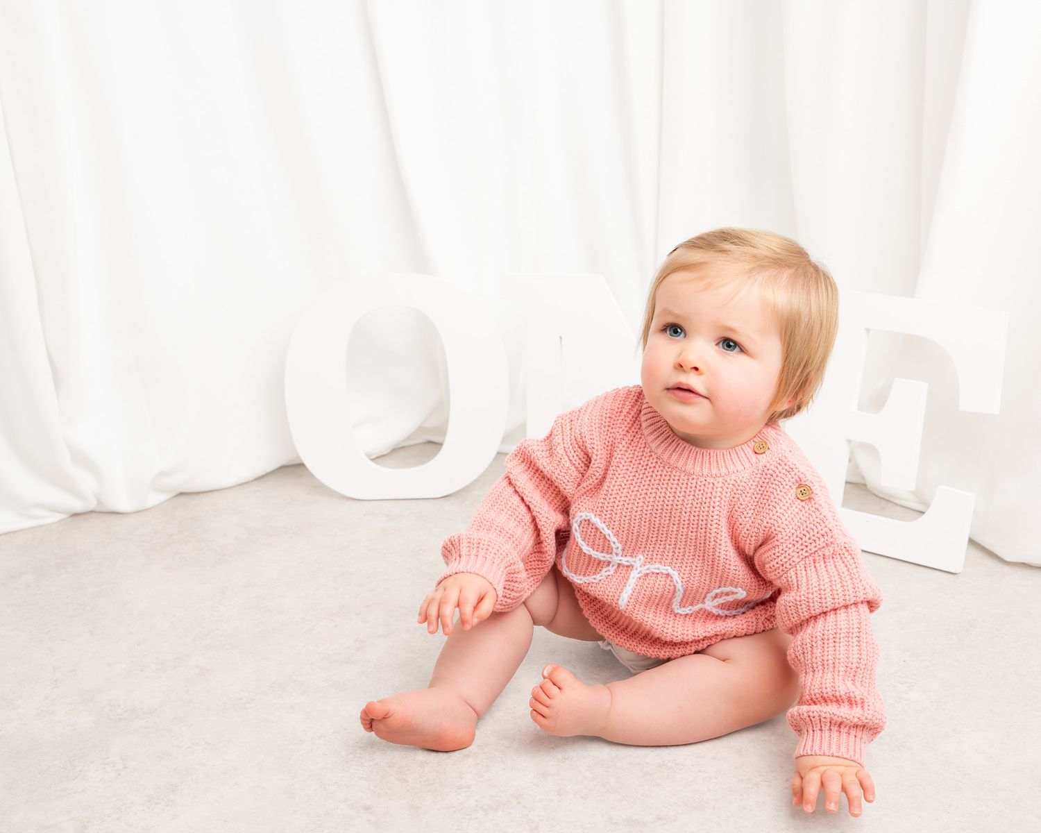 Baby in pink sweater crawling against white background.