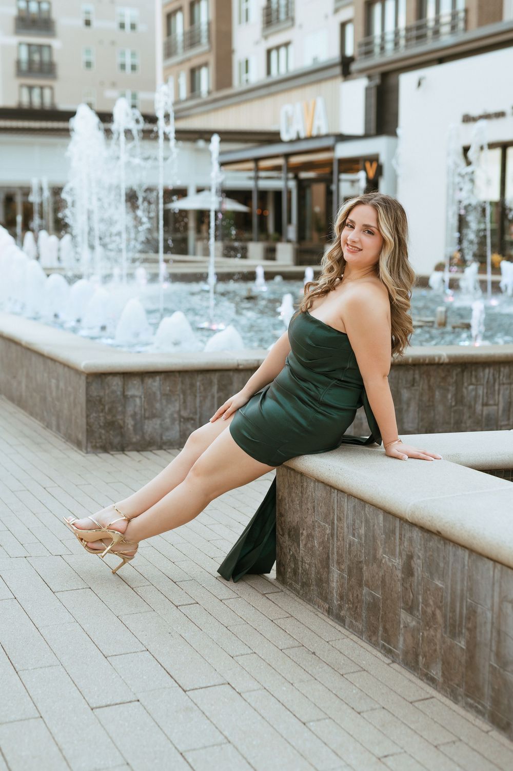 Lifestyle photography session featuring a dark green outfit against a stone wall and fountain backdrop.