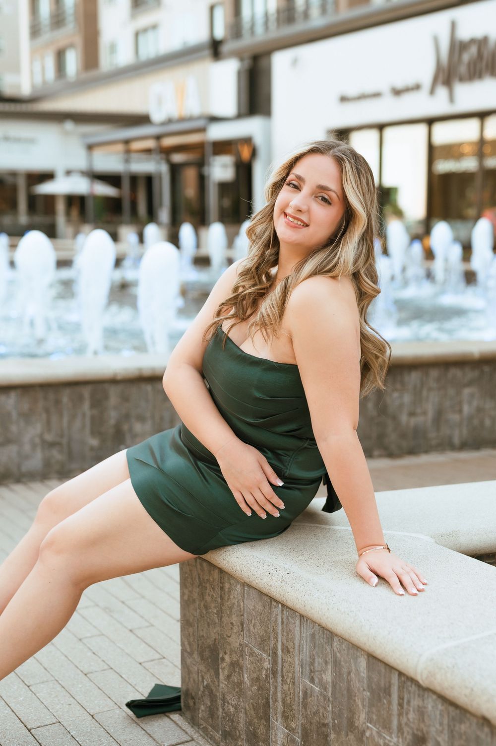 Young woman in a dark green dress poses gracefully on outdoor concrete steps during a photo session.