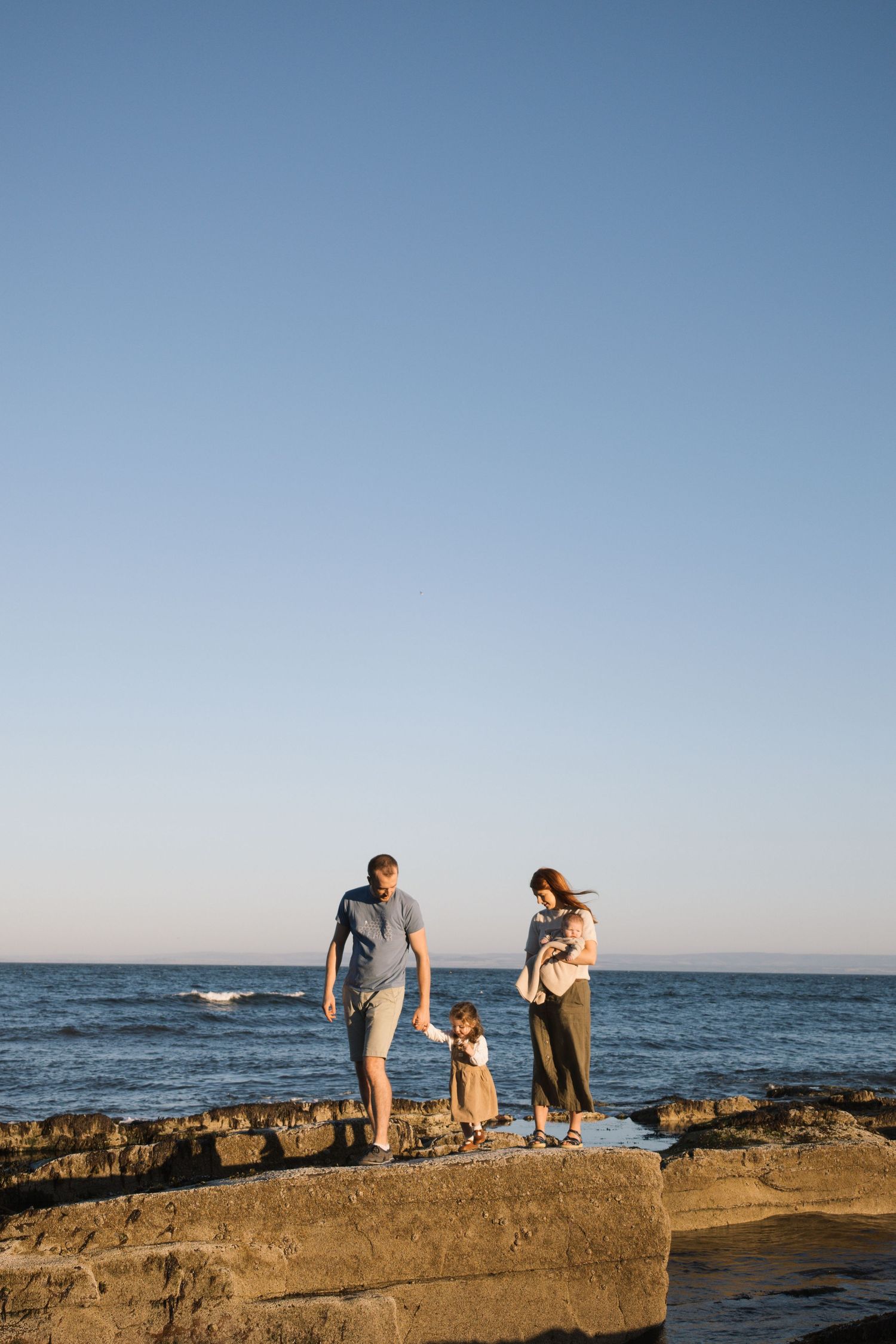 Family sharing candid moments and laughter together in a golden field at sunset with tall grasses swaying in the wind.