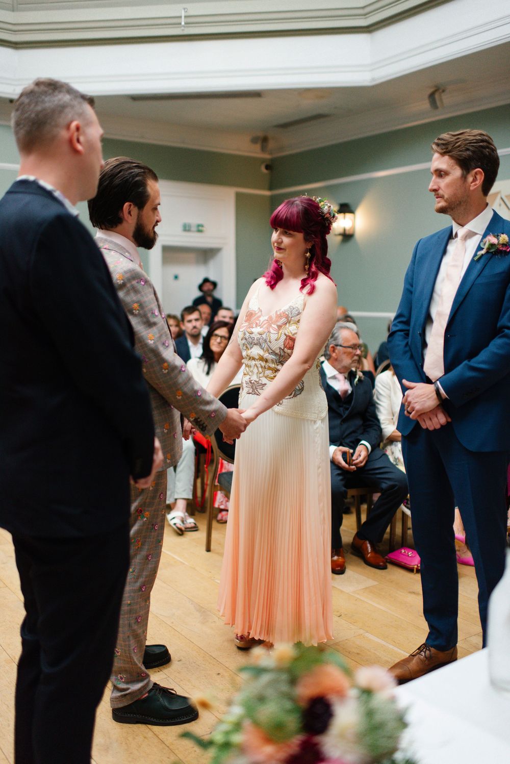 Bride in peach pleated dress holding hands with groom during indoor wedding ceremony at The Hotel Du Vin Brighton.