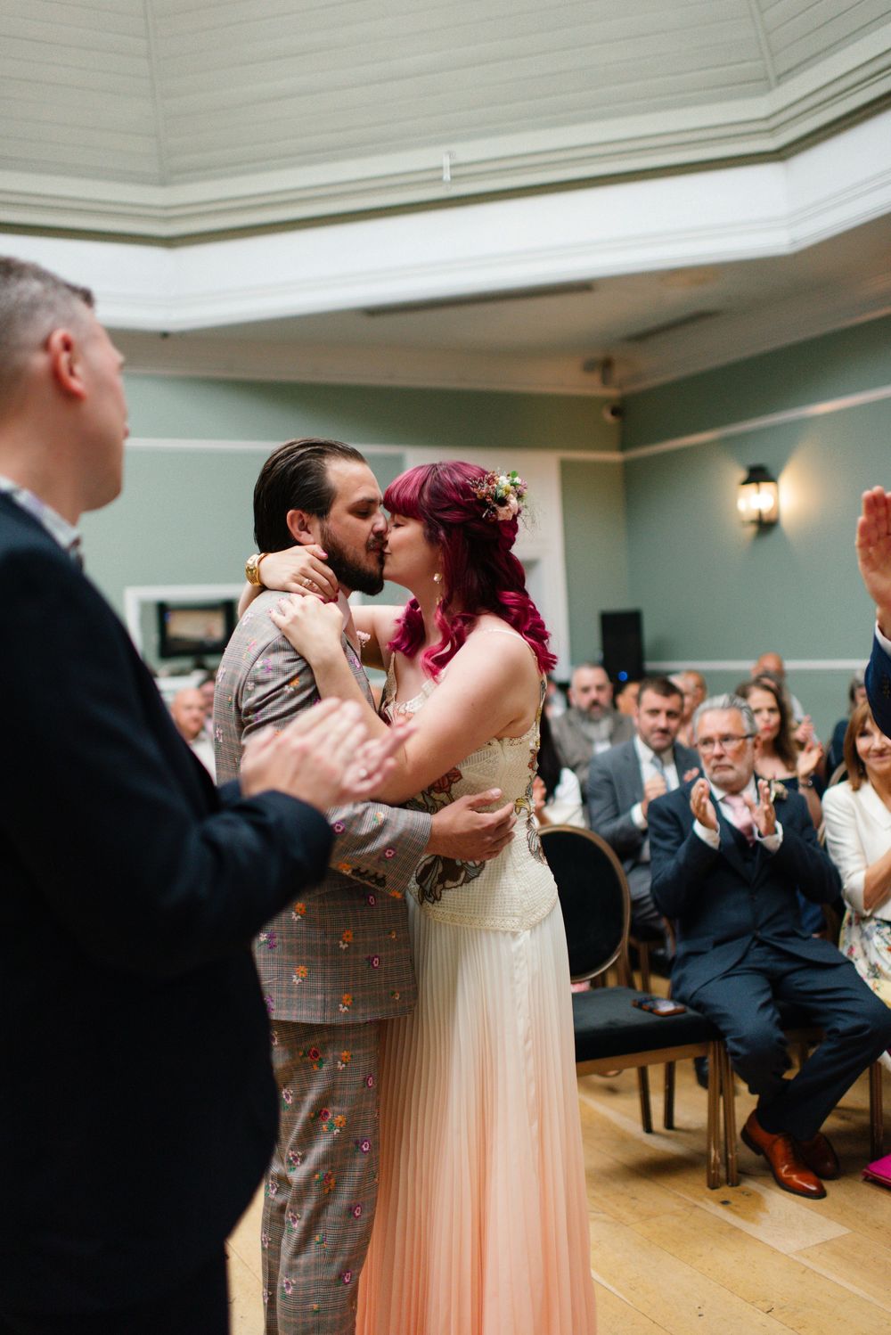 Newlyweds share their first kiss during wedding ceremony as guests applaud in elegant venue at The Hotel Du Vin Brighton.