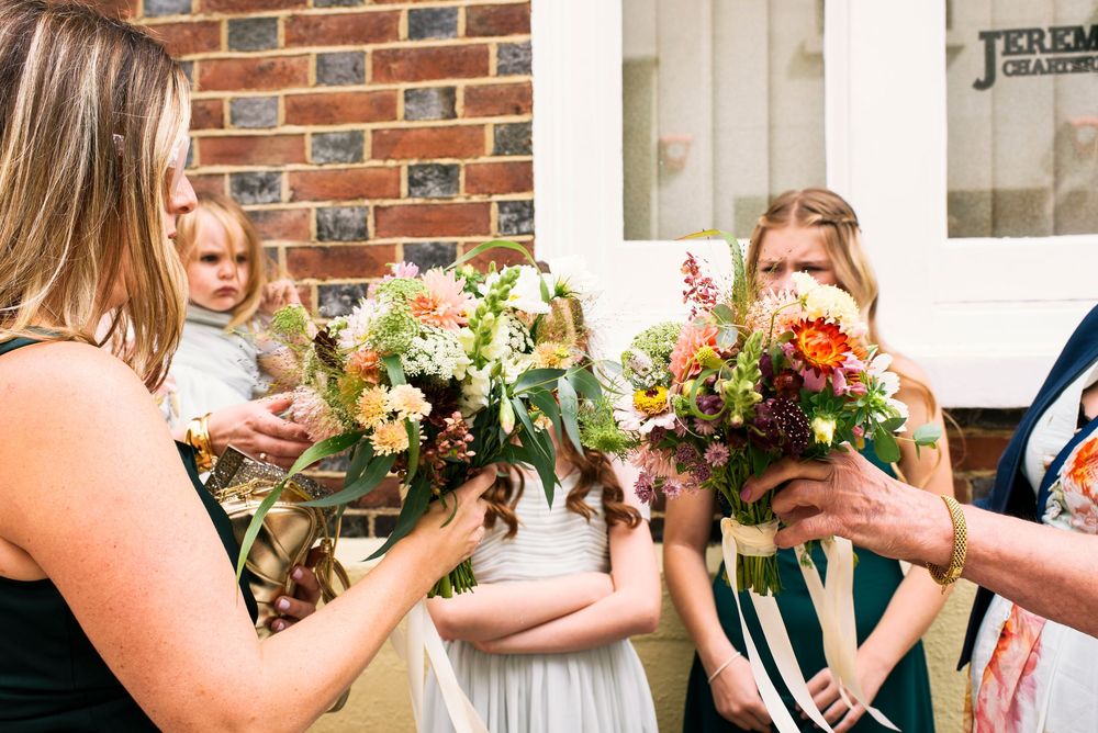 Women and children holding colorful wedding bouquets with autumn flowers outside a brick building.